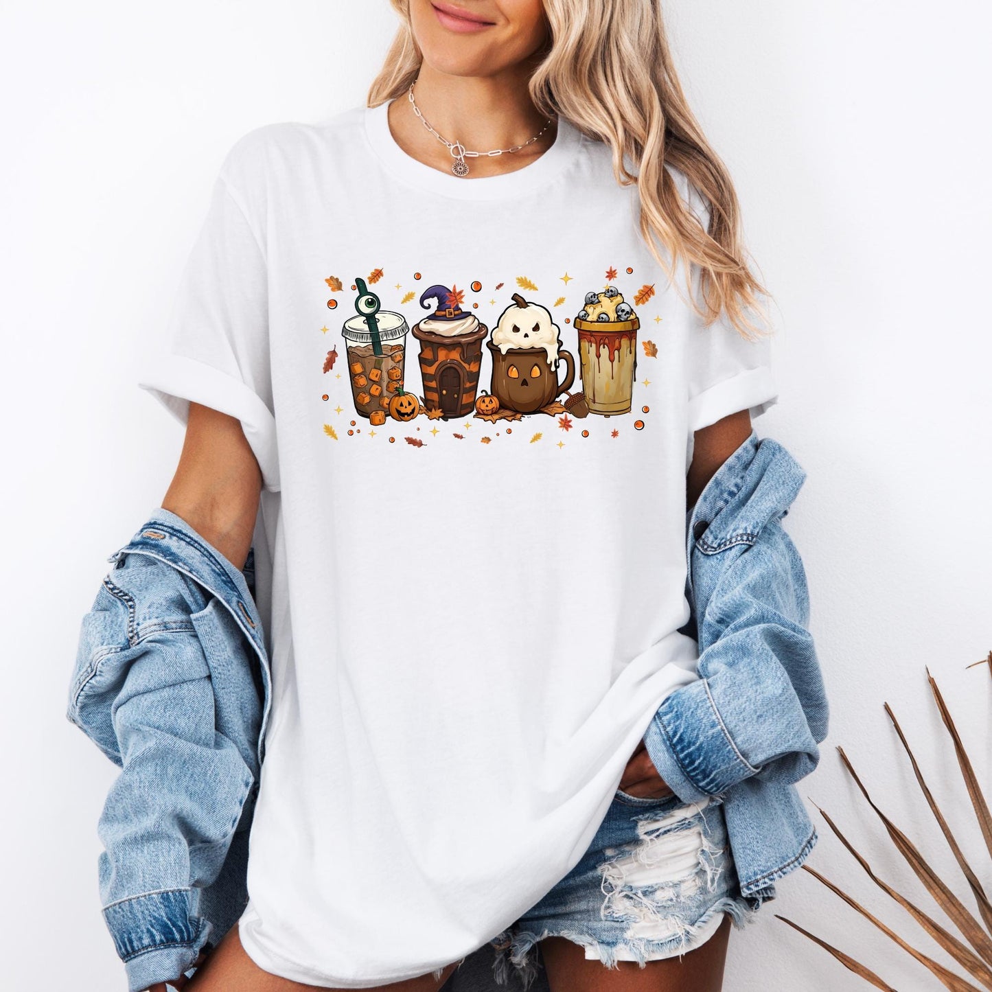 Shirt with a fun Halloween-themed design of five festive drinks, each decorated with spooky details like a witch hat, ghost face, eyeball stirrer, skulls, pumpkins, and dripping syrup, surrounded by autumn leaves and stars.