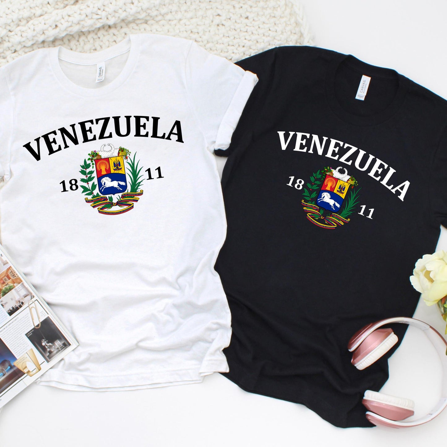 Custom T-shirt design featuring the word “VENEZUELA” in bold black capital letters above the country’s national coat of arms. The coat of arms includes a red, yellow, and blue shield with a white horse, wheat, and weapons, framed by a palm and olive branch. Above the shield is a ribbon in the Venezuelan flag colors (yellow, blue, and red). Below the design, the numbers “18” and “11” are displayed on either side, representing the year 1811.