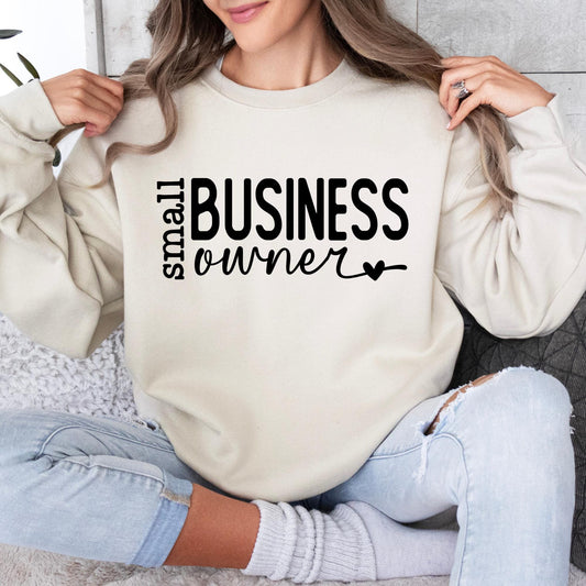 Woman wearing a cream Gildan sweatshirt featuring a minimalist "Small Business Owner" design in black lettering.