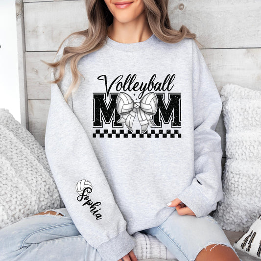 A light gray sweatshirt with &quot;Volleyball MOM&quot; in bold black letters, a Volleyball -patterned bow in the center, a black checkered underline, and a football icon with &quot;Custom Name&quot; written on the sleeve.