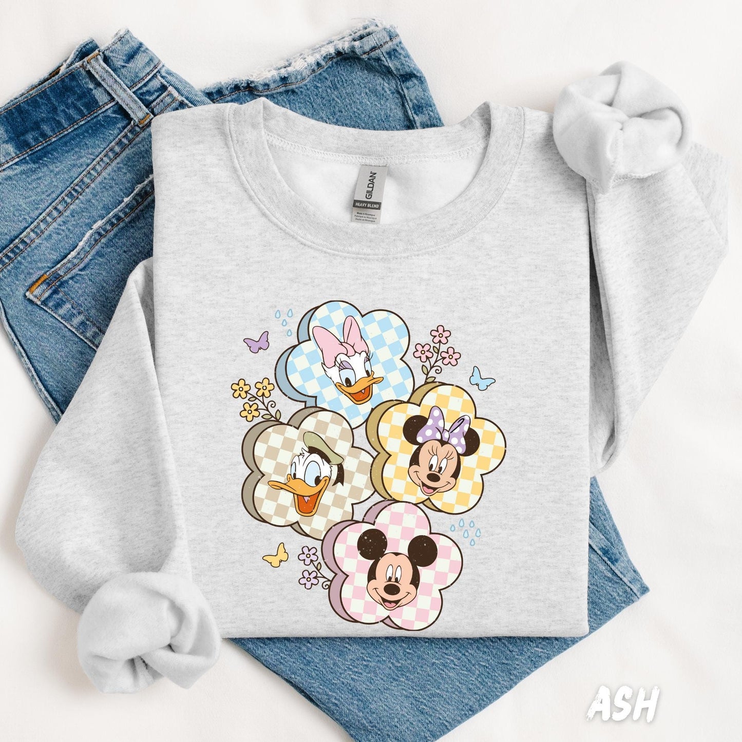 A sweatshirt featuring Mickey, Minnie, Donald, and Daisy in gingham flower frames, surrounded by small flowers and butterflies for a cute, playful design.