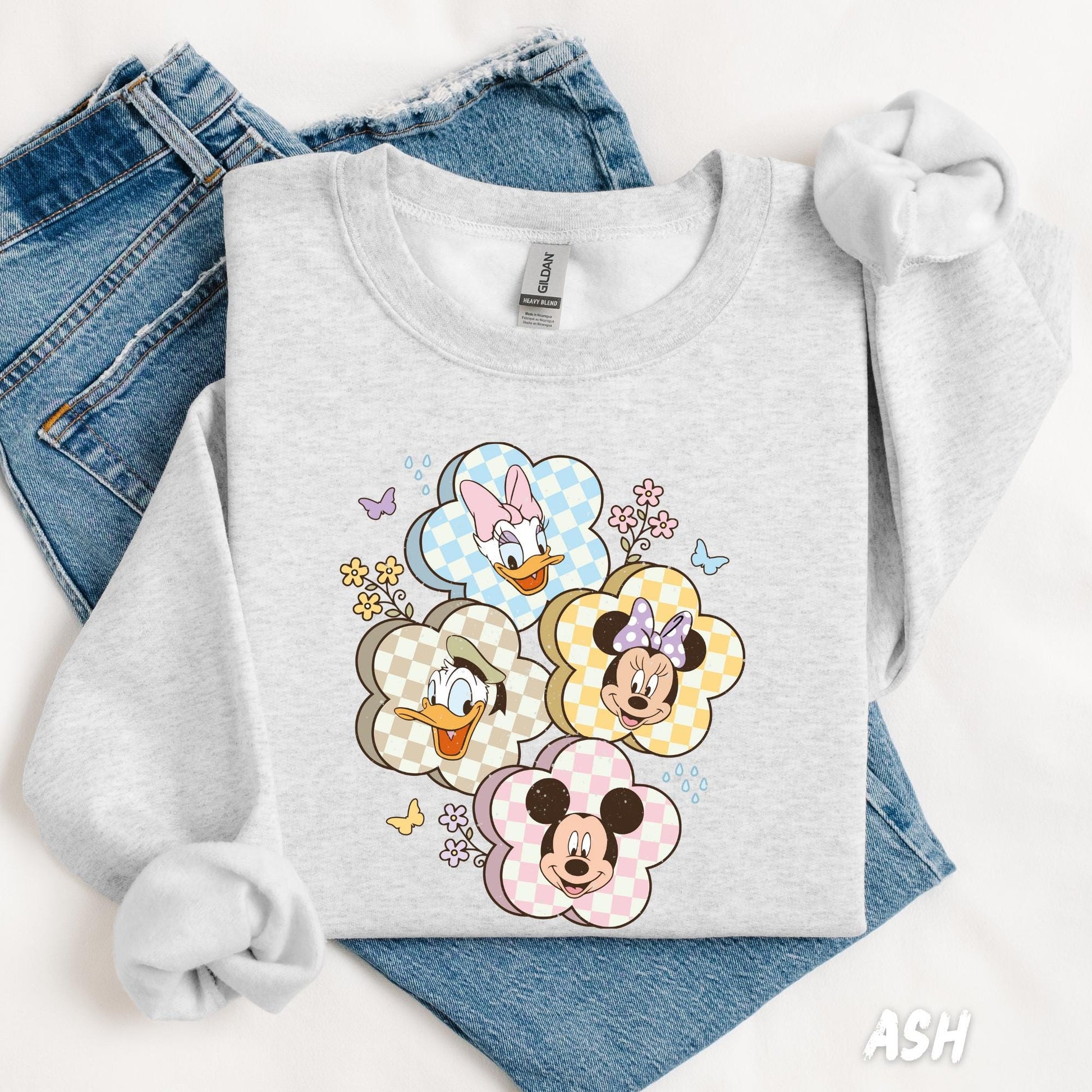 A sweatshirt featuring Mickey, Minnie, Donald, and Daisy in gingham flower frames, surrounded by small flowers and butterflies for a cute, playful design.