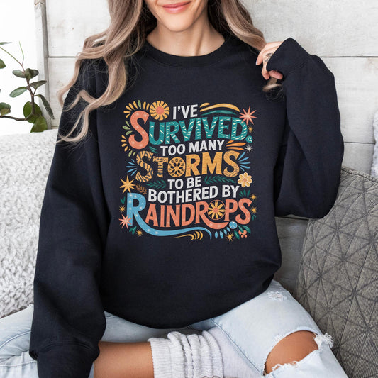 A bold, colorful typographic design with floral and decorative accents featuring the quote: &quot;I&#39;ve survived too many storms to be bothered by raindrops,&quot; in vibrant orange, teal, and yellow tones.