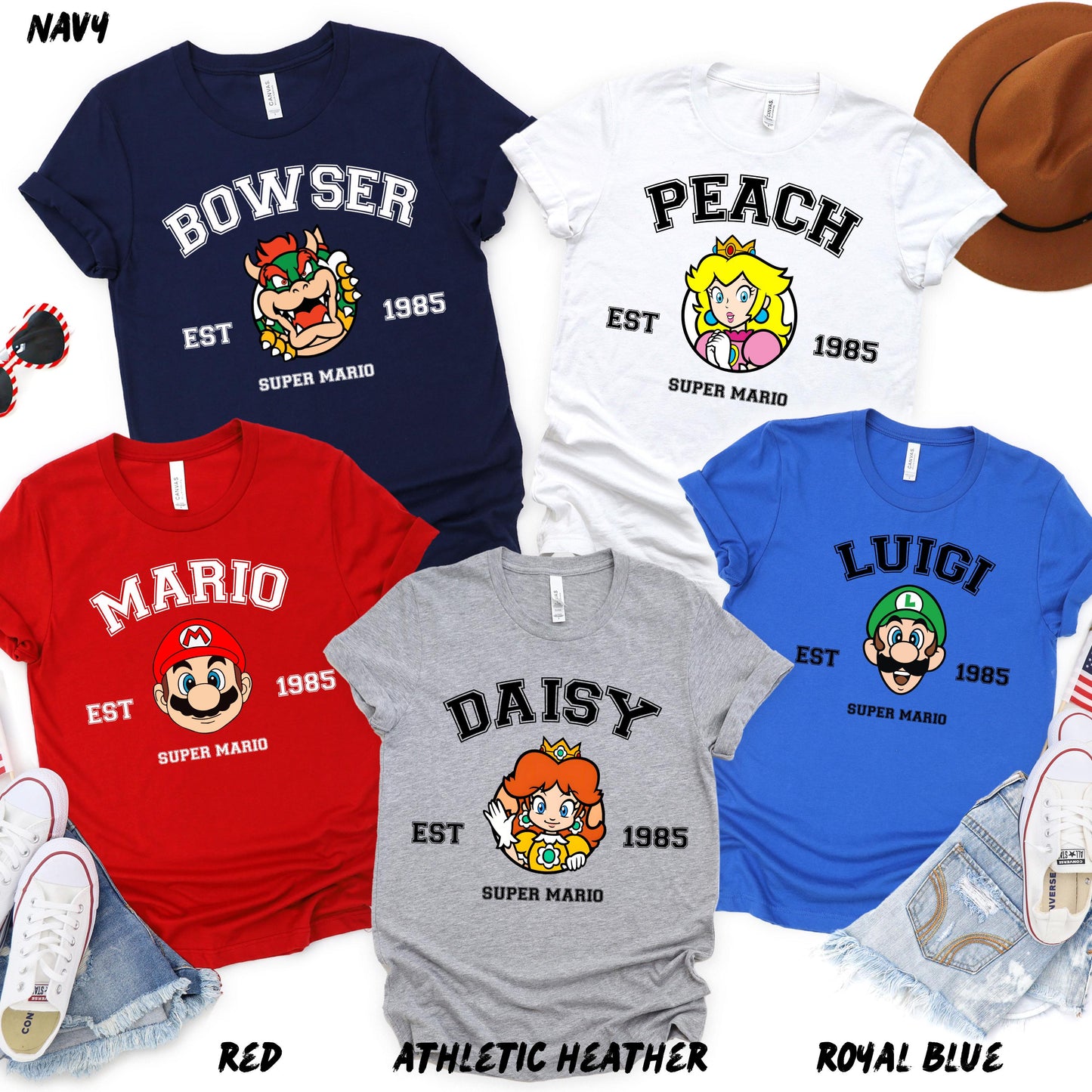 A set of five colorful T-shirts featuring Super Mario characters: Mario (red), Luigi (blue), Peach (white), Daisy (gray), and Bowser (navy). Each shirt has "EST 1985" and "Super Mario" text.