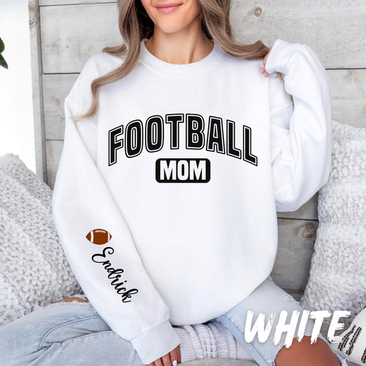 A women sweatshirt with bold black text reading &quot;FOOTBALL MOM&quot; on the front. The left sleeve features a small football graphic and the custom name in cursive.