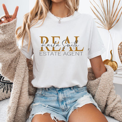 T-shirt featuring a design that reads "REAL ESTATE AGENT" in bold, gold and black uppercase letters. The custom real esta name written in an elegant cursive script overlaying the word "REAL."