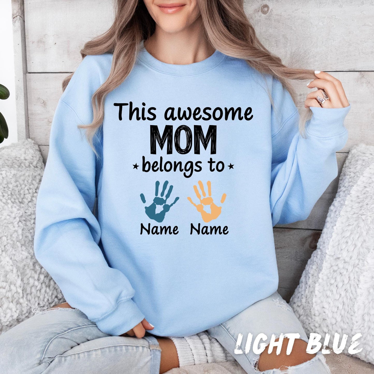 sweatshirt with the text "This awesome MOM belongs to" printed on it. Below the text is a blue handprint graphic and the custom kids name.