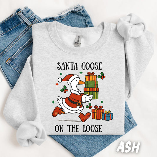 Ash gray unisex sweatshirt featuring a fun design of a goose dressed as Santa running with Christmas presents. Surrounded by holly, stars, and the phrase “Santa Goose On The Loose” in playful black text. A quirky and festive holiday pullover.