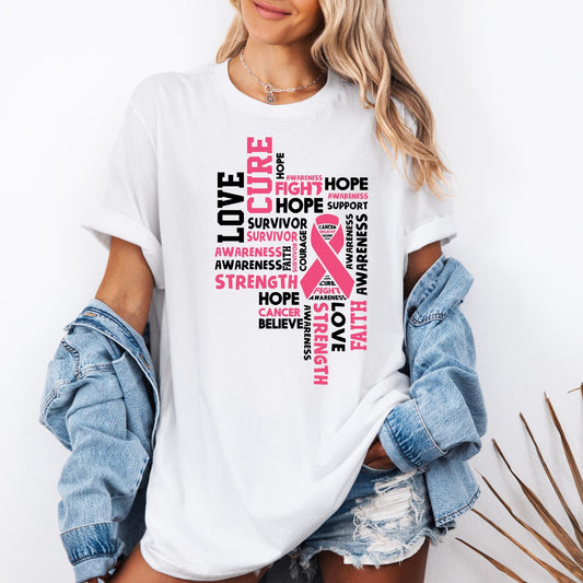 t-shirt with a bold breast cancer awareness design printed on the front. The print features a large pink ribbon made up of powerful words such as Love, Cure, Strength, Faith, Survivor, Awareness, Hope, Courage, and Believe. The text is arranged in different fonts and directions, creating a striking word art effect that emphasizes support, strength, and awareness for breast cancer