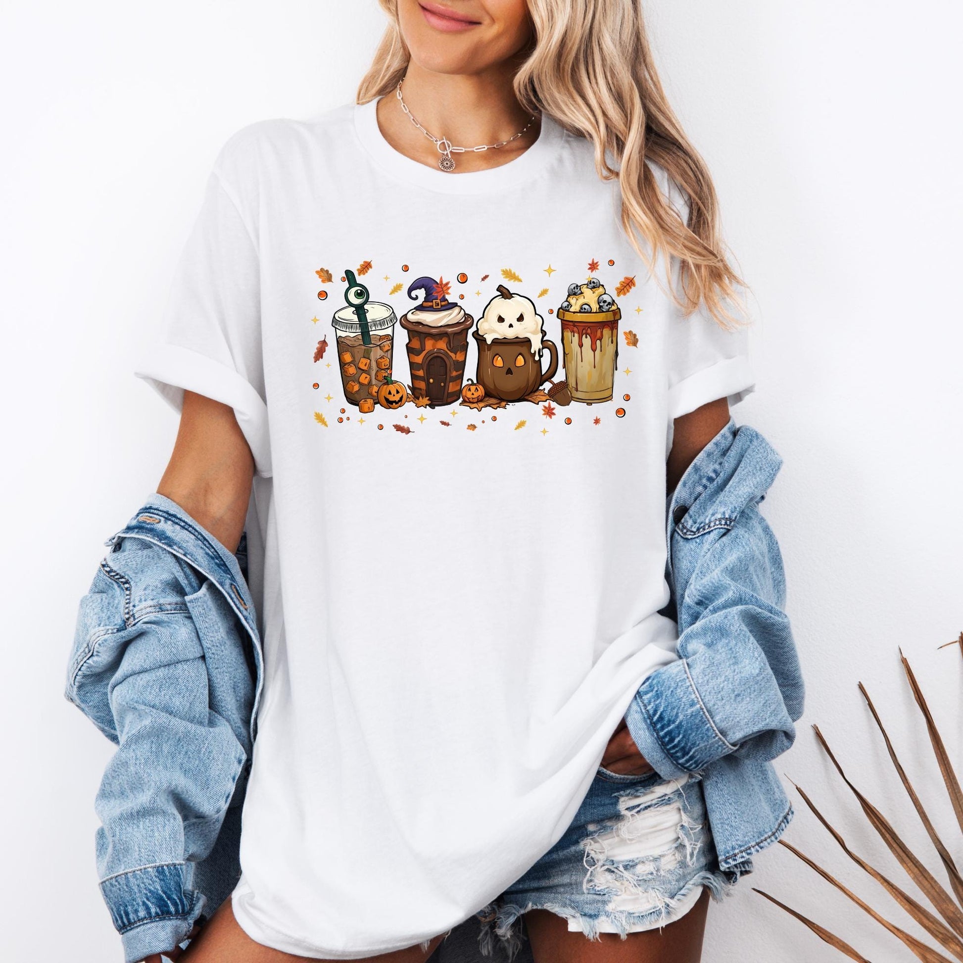 Shirt with a fun Halloween-themed design of five festive drinks, each decorated with spooky details like a witch hat, ghost face, eyeball stirrer, skulls, pumpkins, and dripping syrup, surrounded by autumn leaves and stars.