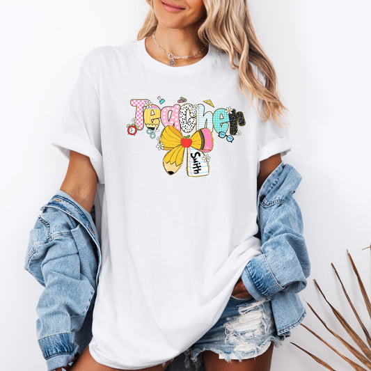 Custom teacher shirt featuring the word &quot;Teacher&quot; in colorful, playful school-themed letters with a yellow pencil bow and customizable name tag – perfect back-to-school or teacher appreciation gift.