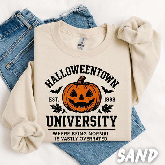 sweatshirt with a bold black Halloween-themed university-style design. At the center is a carved jack-o&#39;-lantern pumpkin with bats and autumn leaves around it. Above the pumpkin, the text reads “Halloweentown University” in collegiate font, with “Est. 1998” on either side. Below it, the phrase “Where being normal is vastly overrated” is written in smaller letters.