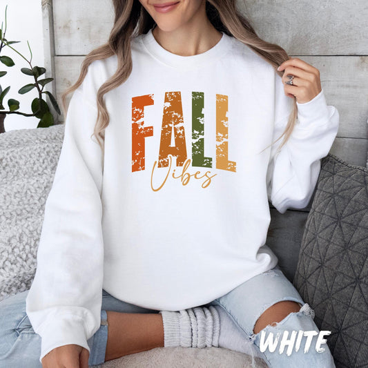 White unisex fall sweatshirt with “FALL Vibes” text in rustic orange, green, and brown distressed lettering. Cozy autumn sweater for adults and kids, available in multiple colors—perfect for Thanksgiving, pumpkin patch outings, and cozy fall vibes.