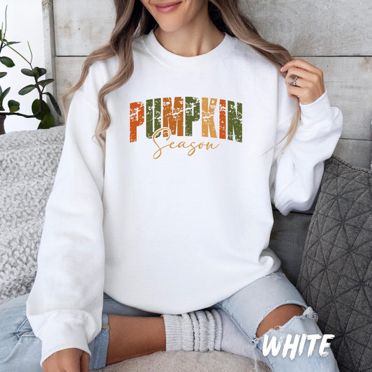 White unisex sweatshirt with “PUMPKIN Season” text in distressed fall colors (orange, green, and brown). Cozy autumn sweater for adults and kids, available in various colors—perfect for pumpkin patch trips and Thanksgiving.