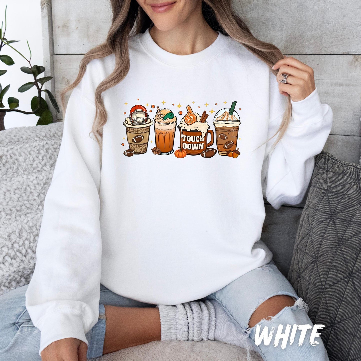 White unisex sweatshirt with fun fall coffee drinks featuring football-themed toppings, whipped cream, and "TOUCHDOWN" mug design. A cozy pullover for coffee lovers and game day fans—available in multiple colors for adults and kids.