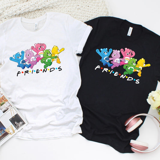 Alt text: Graphic t-shirt featuring a colorful group of cartoon bears in blue, pink, green, purple, and yellow, standing together above the word “FRIENDS” in a playful font with multicolored dots between the letters, inspired by the classic TV show logo.