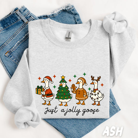 unisex sweatshirt featuring four cartoon Christmas geese dressed as Santa, a Christmas tree, a gingerbread cookie, and a reindeer. Below, the phrase “Just a Jolly Goose” in playful script. A fun and quirky holiday pullover.