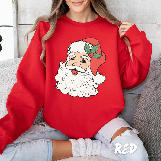 Woman wearing a red Christmas sweatshirt featuring a vintage-style Santa Claus face with a holly decoration on his hat, sitting comfortably in a cozy setting.