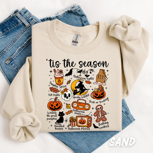 Unisex sweatshirt with a fun Halloween-themed design titled "’Tis the Season" featuring a collection of cute seasonal illustrations including a pumpkin spice drink, witch on the moon, gravestone, pumpkins, bats, skeleton, haunted house, black cat, and phrases like “Fall Nights,” “Trick or Treating,” and “Halloween Movies,” all arranged in a playful collage.