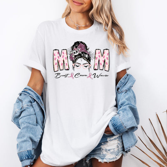 t-shirt with a design that says “MOM Breast Cancer Warrior” in bold letters filled with pink ribbons. The center features a graphic of a woman with a bun, pink bow, and glasses, symbolizing strength and awareness for breast cancer.