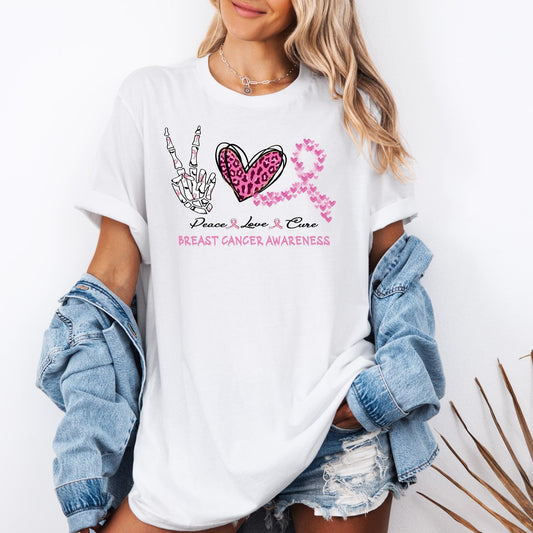 t-shirt with “Peace Love Cure Breast Cancer Awareness” graphic. The design features a skeleton hand making a peace sign, a pink leopard print heart, and a breast cancer awareness ribbon made of small pink hearts, symbolizing support and hope.