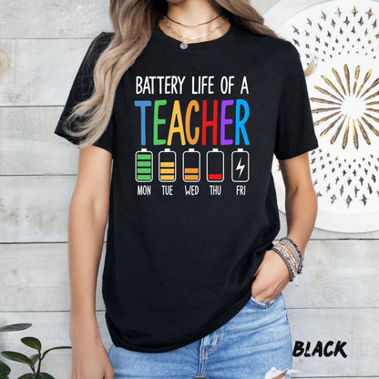 t-shirt featuring the phrase 'Battery Life of a Teacher' in bold white and colorful text. Below, five battery icons represent the week: Monday full green, Tuesday yellow, Wednesday half orange, Thursday low red, and Friday empty with a lightning bolt. The word 'TEACHER' is printed in rainbow colors."