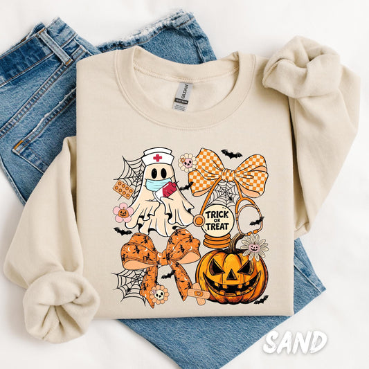 sweatshirt folded with denim jeans, featuring a cute Halloween design. The graphic includes a ghost dressed as a nurse with a face mask and clipboard, surrounded by orange plaid and Halloween-patterned bows, spiderwebs, a stethoscope, flowers, a jack-o’-lantern, and the phrase &quot;Trick or Treat.