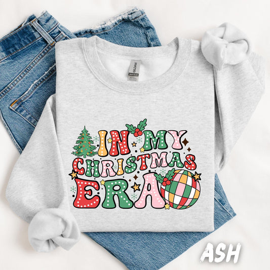 Unisex light ash gray Christmas sweatshirt with colorful retro “In My Christmas Era” design featuring festive letters, stars, holly leaves, Christmas tree, and plaid ornament. Cozy cotton-poly blend holiday sweater, perfect for the Christmas season or as a cute winter gift.