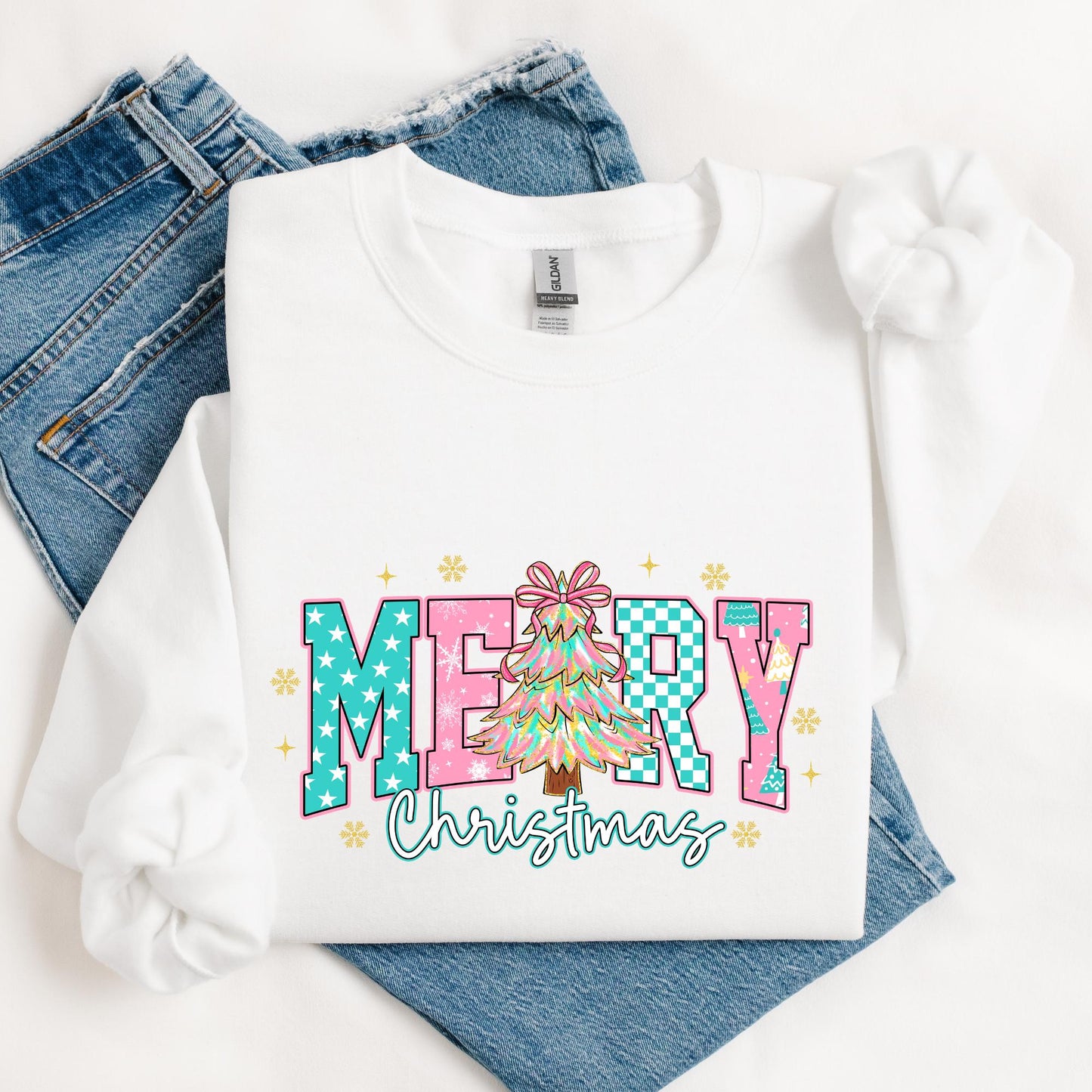 White sweatshirt with colorful “Merry Christmas” design in pastel pink, teal, and aqua tones, featuring a festive Christmas tree with a pink bow in the center.