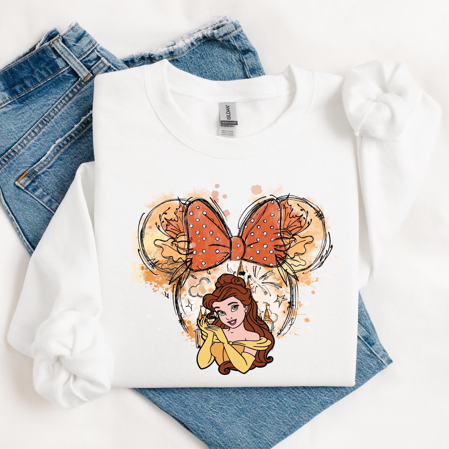 A sweatshirt featuring a watercolor-style Minnie Mouse ears design with a polka-dotted bow, accented with floral details. Below, Belle Princess from Disney's Movie