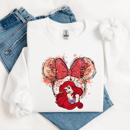 A sweatshirt featuring a watercolor-style Minnie Mouse ears design with a polka-dotted bow, accented with floral details. Below, The Little Mermaid Princess from Disney's Movie