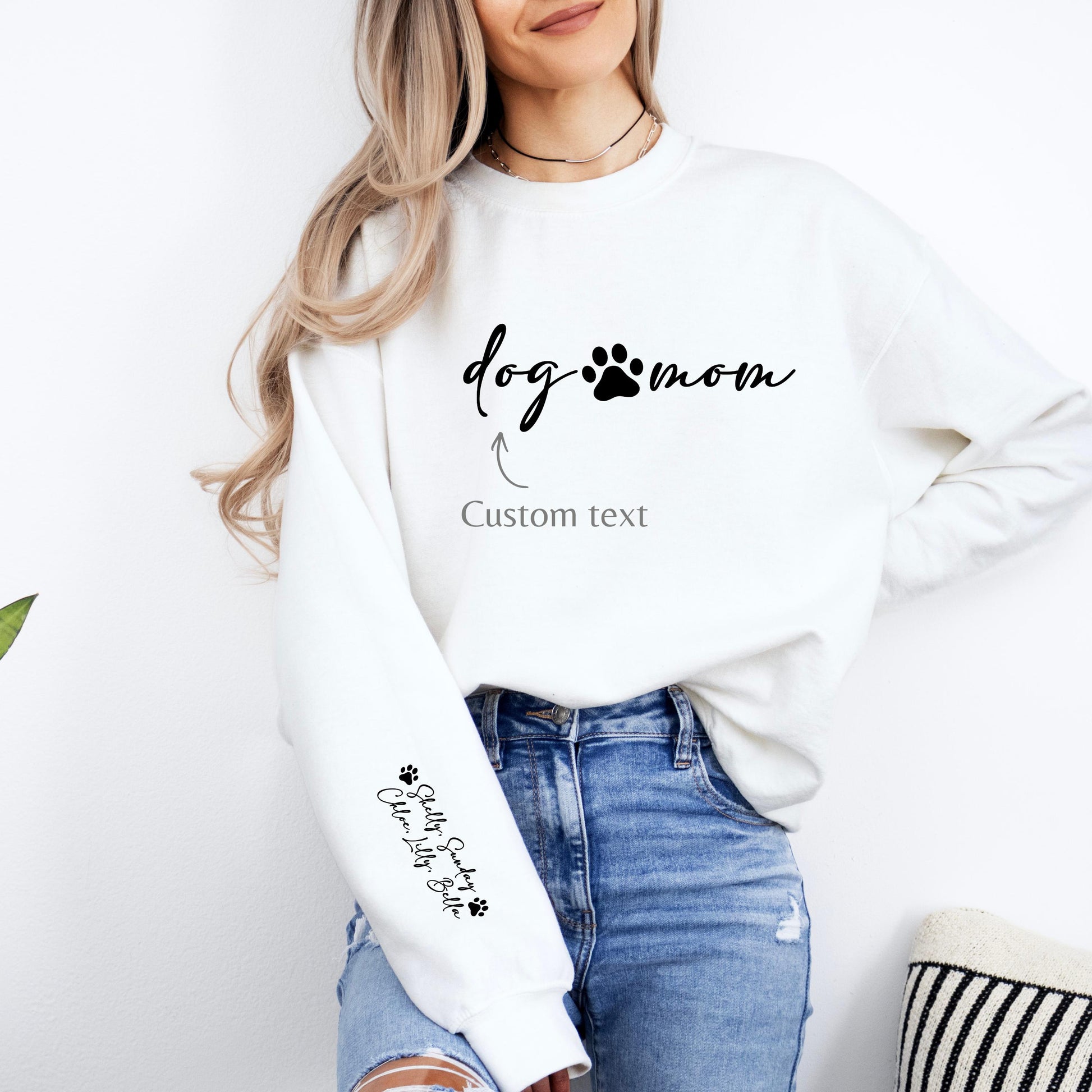 cozy sweatshirt for dog lovers with “dog mom” text and paw print on the chest, customizable wording, and personalized pet names printed on the sleeve. Casual women’s pet mom sweatshirt styled with jeans.