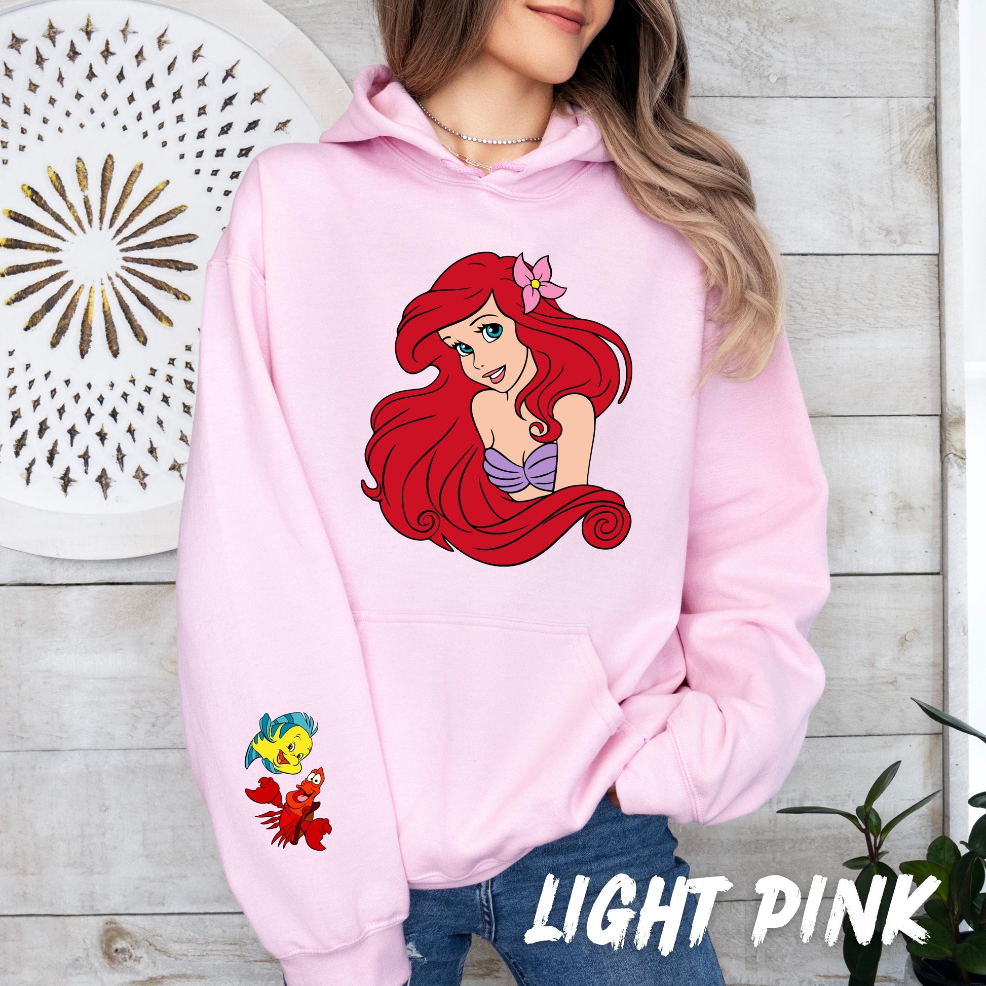 sweatshirt with a graphic of Ariel, the Little Mermaid, with a purple seashell bra and a pink flower in her hair.  The graphic also includes Flounder, Ariel's yellow and blue fish friend, and Sebastian, the red crab.