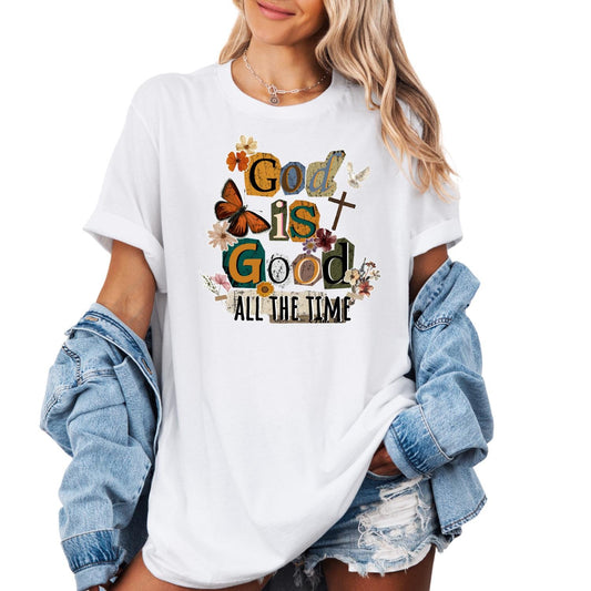 unisex t-shirt featuring a colorful vintage-style typography design that reads “God is Good All the Time,” decorated with floral elements, butterflies, and a cross, styled on a woman wearing denim shorts and a light blue jean jacket against a clean white background.