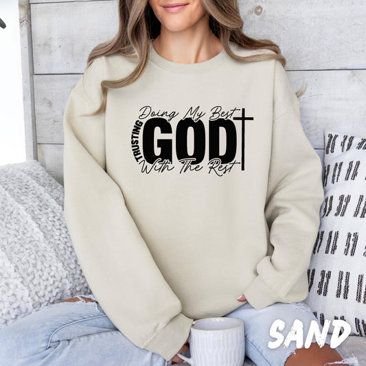 crewneck sweatshirt with black Christian typography reading “Doing My Best Trusting God With The Rest,” featuring a cross design, styled with blue jeans for a casual faith-inspired look.