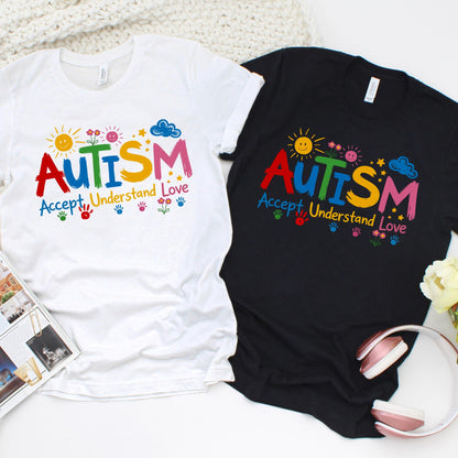 Autism awareness shirt with colorful “AUTISM Accept Understand Love” design featuring sun, flowers, stars, and handprints on white and black t-shirts flat lay.