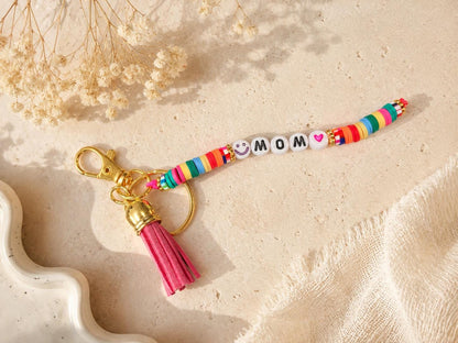 Personalized colorful beaded keychain with tassel attached to a beige backpack zipper, handmade custom name accessory gift.