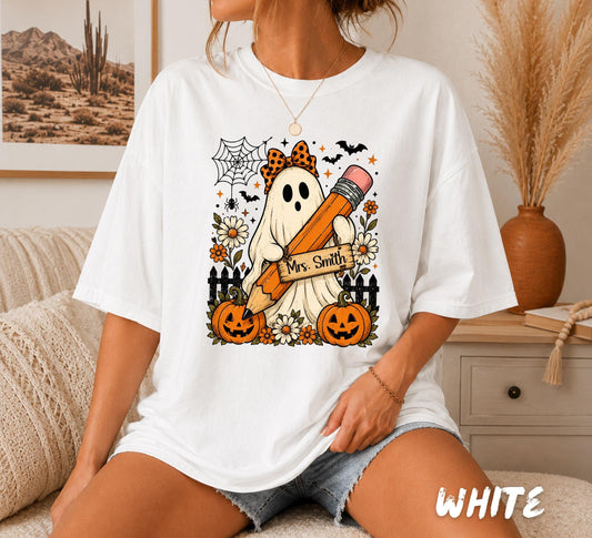 Comfort Colors 1717 white teacher Halloween shirt featuring a personalized ghost holding a pencil with custom teacher name, pumpkins, flowers, bats, spiderweb, and cute spooky classroom design.