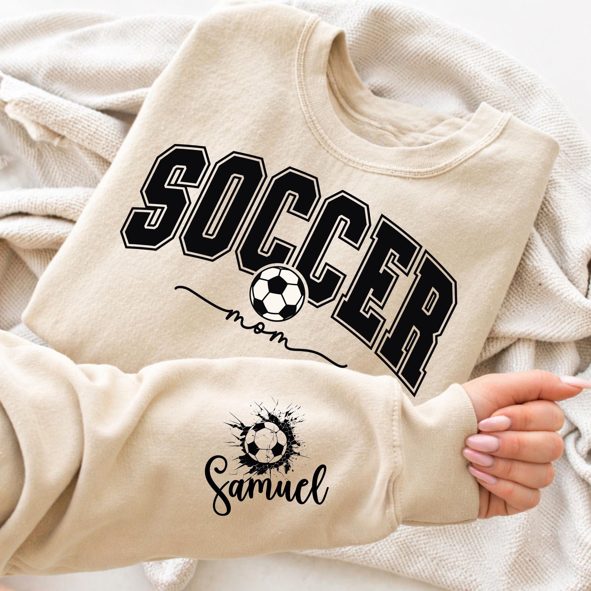 Sand Gildan crewneck sweatshirt featuring a personalized Soccer Mom design with customizable player name, perfect for game days and soccer season.