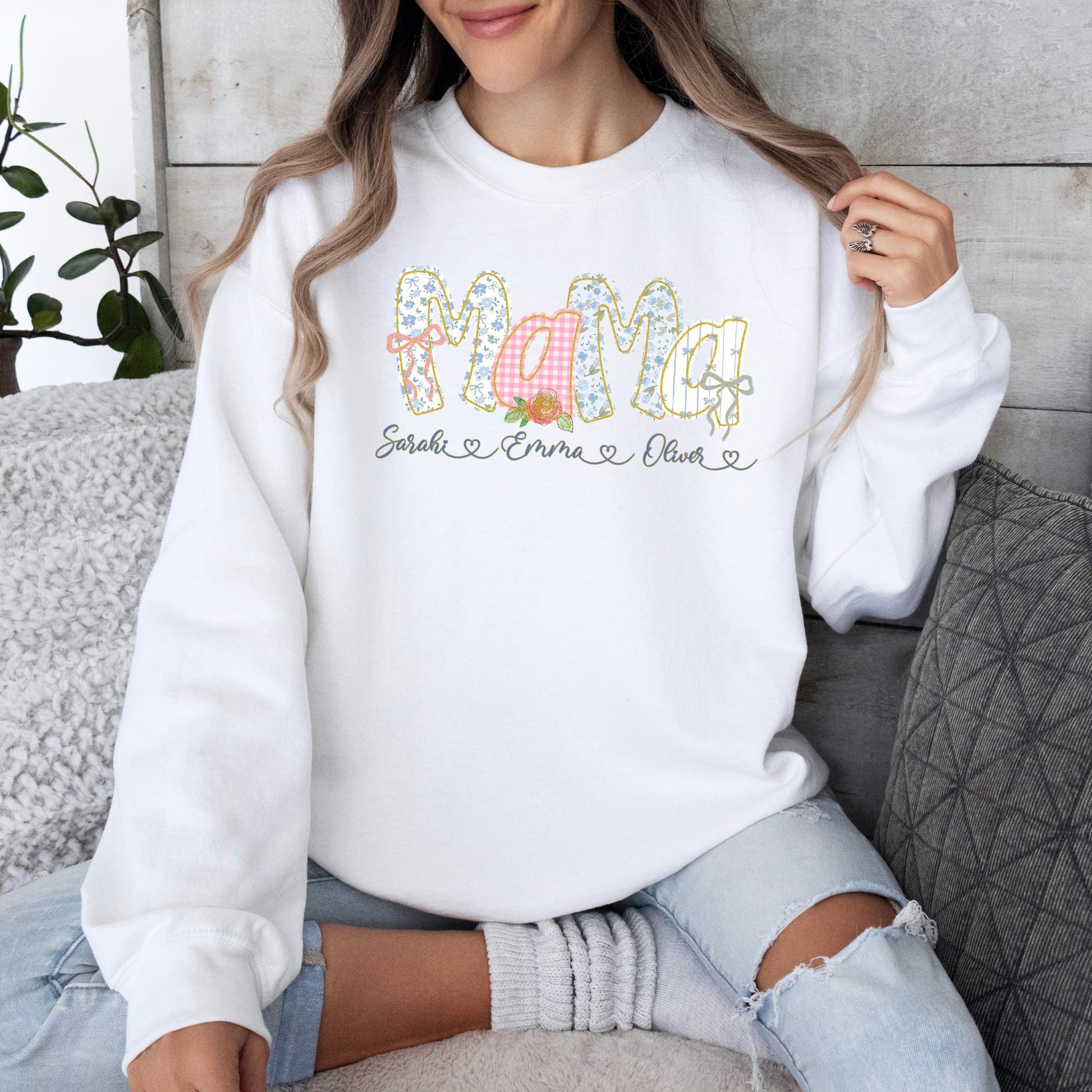 May include: White sweatshirt with the word "Mama" in a floral and gingham design. The names "Sarah", "Emma", and "Oliver" are printed below the word "Mama".