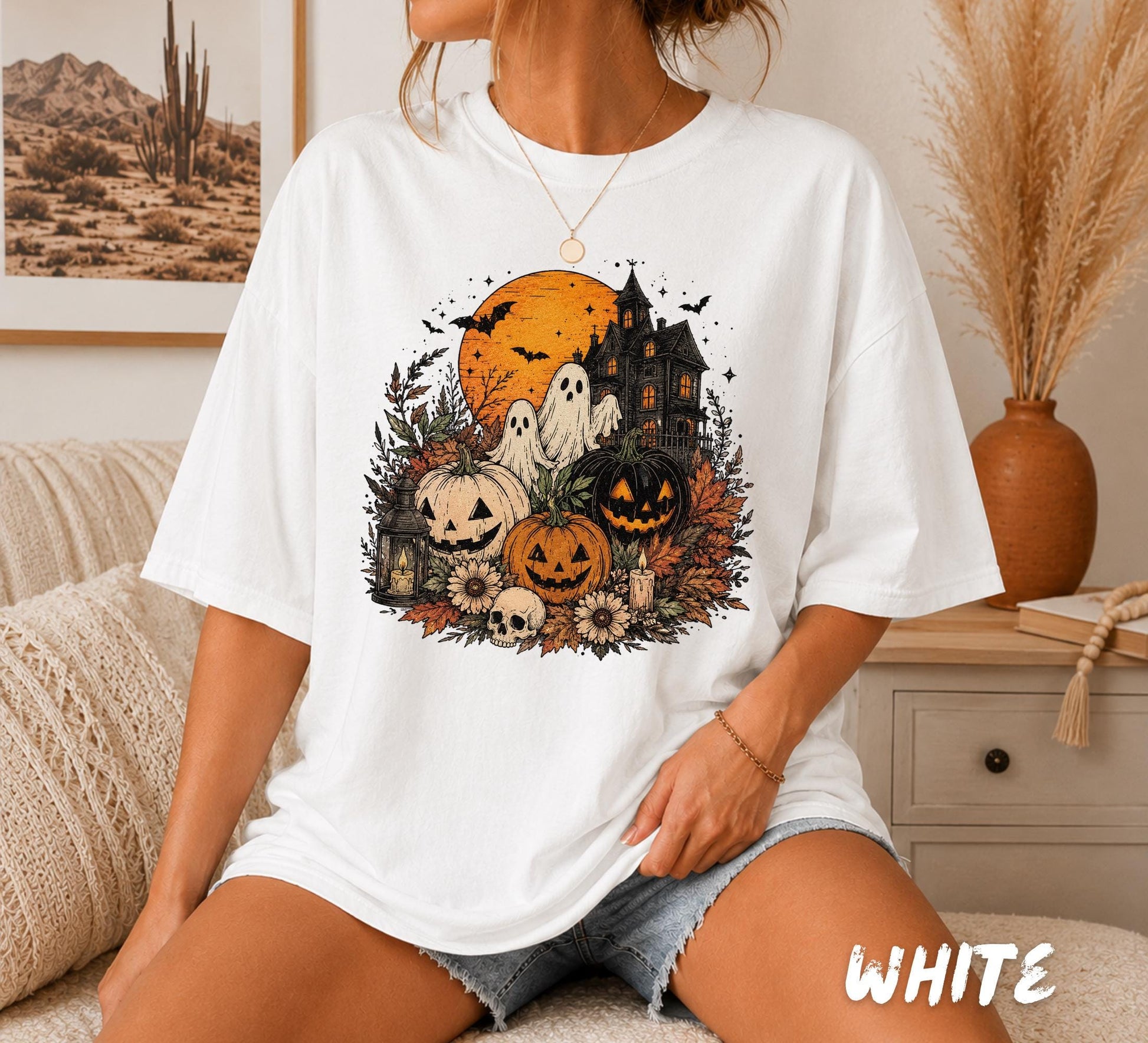 Comfort Colors white t-shirt featuring a vintage Halloween design with ghosts, carved pumpkins, haunted house, full moon, candles, autumn leaves, skull, and cozy fall aesthetic.