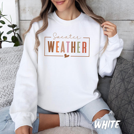White unisex sweatshirt with “Sweater WEATHER” design in multicolor fall tones and a small heart detail. Cozy autumn pullover for adults and kids, perfect for fall weather, Thanksgiving, and casual seasonal outfits. Available in a variety of colors.