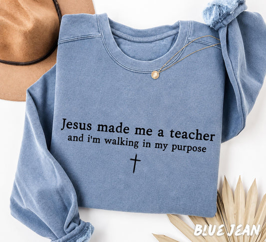 Folded Blue Jean Comfort Colors sweatshirt featuring the Christian teacher quote "Jesus Made Me A Teacher And I'm Walking In My Purpose" with a simple cross design.