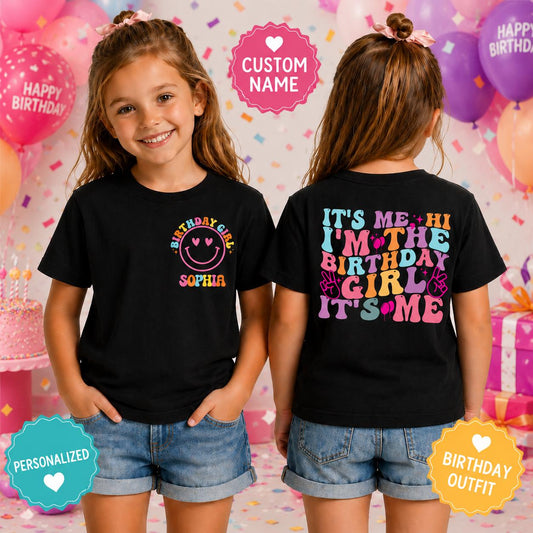Young girl wearing a personalized black birthday shirt with a custom name smiley face design on the front and a colorful "It's Me Hi I'm The Birthday Girl" graphic on the back.