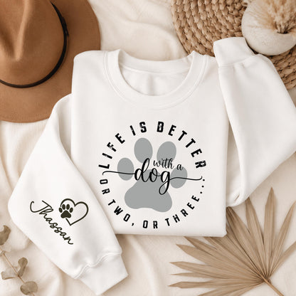 White Gildan crewneck sweatshirt featuring a "Life Is Better With a Dog" graphic with a paw print and personalized pet name on the sleeve, perfect for dog lovers.