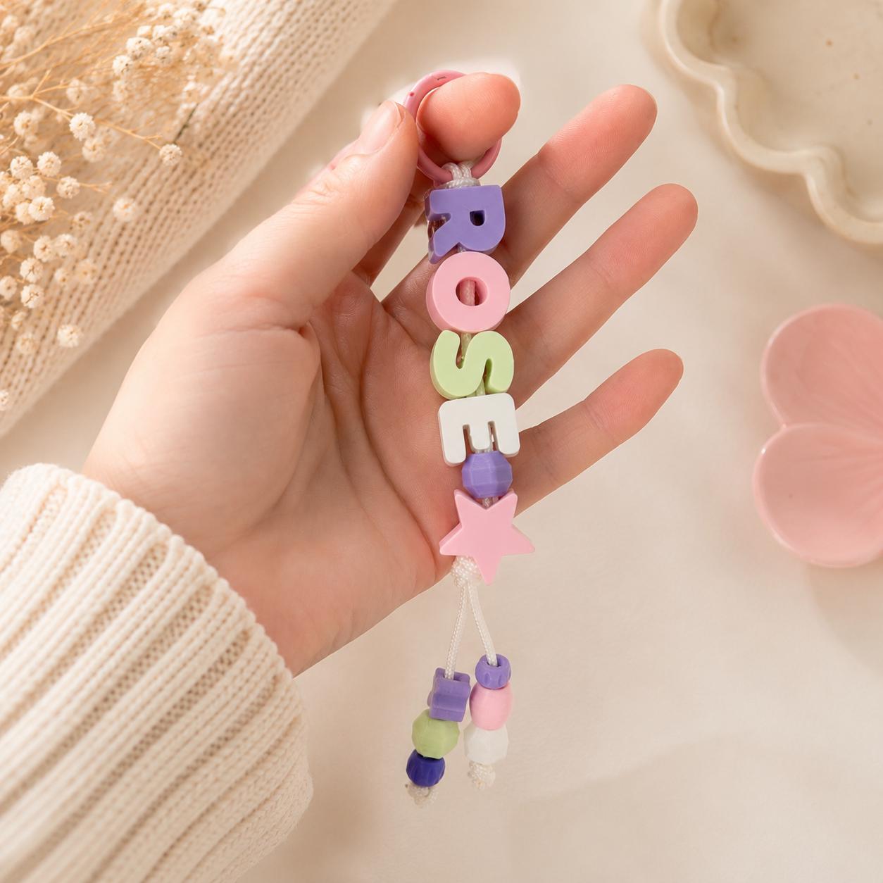 Close-up of a custom ROSE keychain featuring pastel PLA letter beads, pink ring, star charm, and decorative bead tassels.