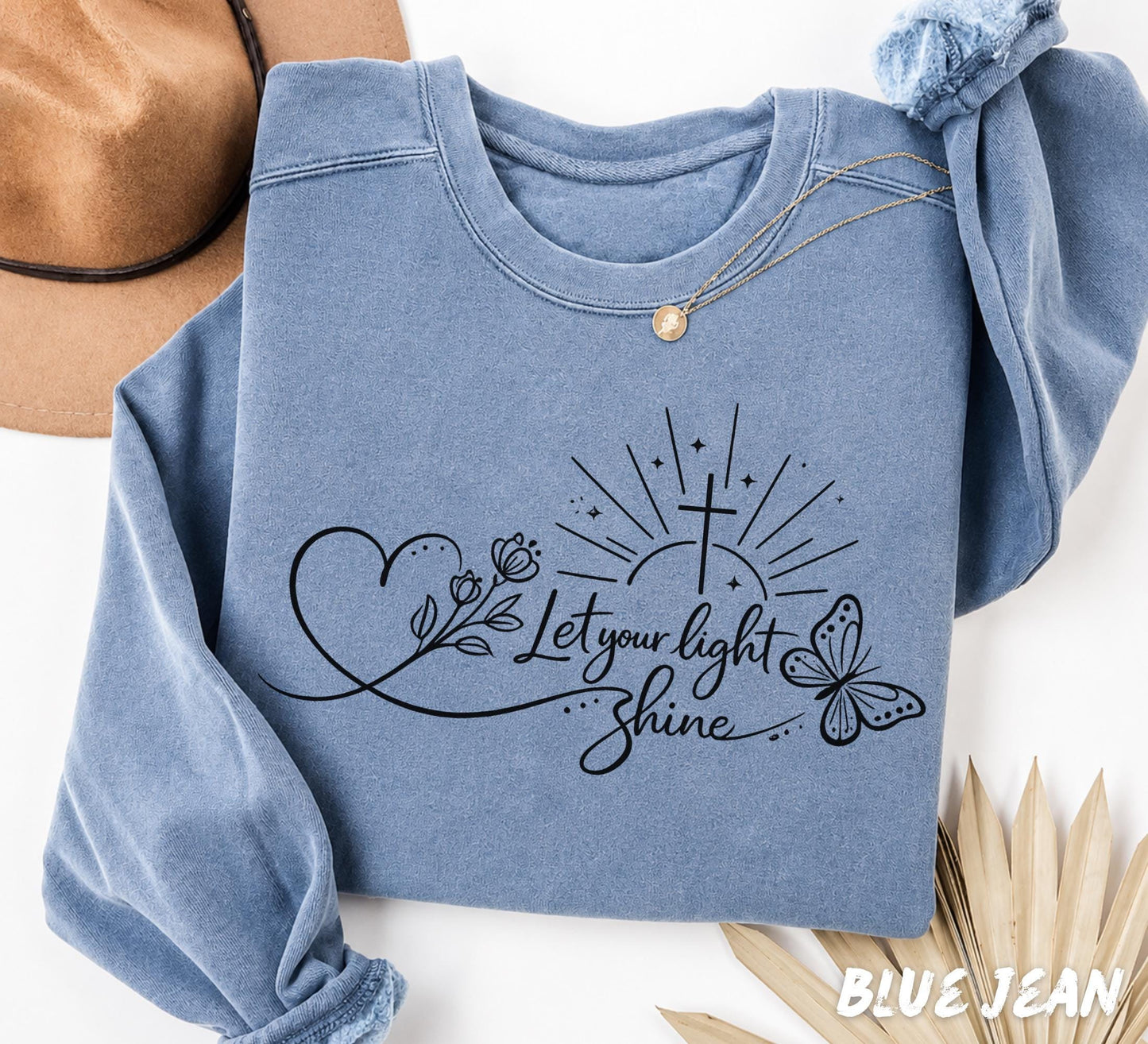 Folded blue Comfort Colors sweatshirt featuring Let Your Light Shine Christian butterfly floral graphic