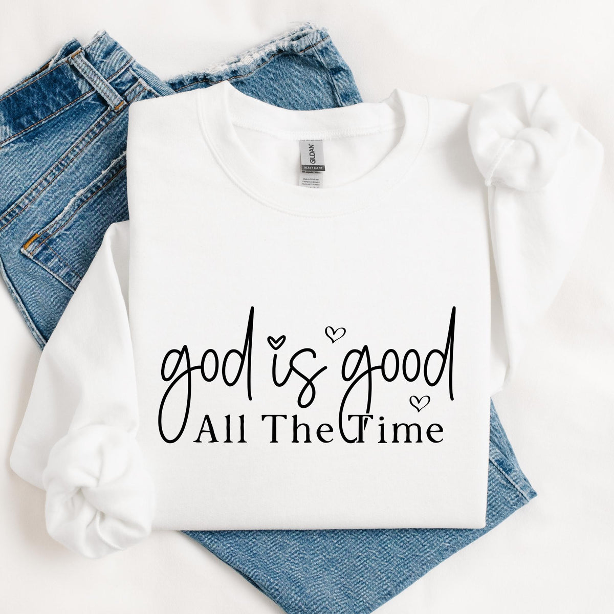 White crewneck sweatshirt featuring a black “God Is Good All The Time” Christian faith design with handwritten lettering and small hearts.