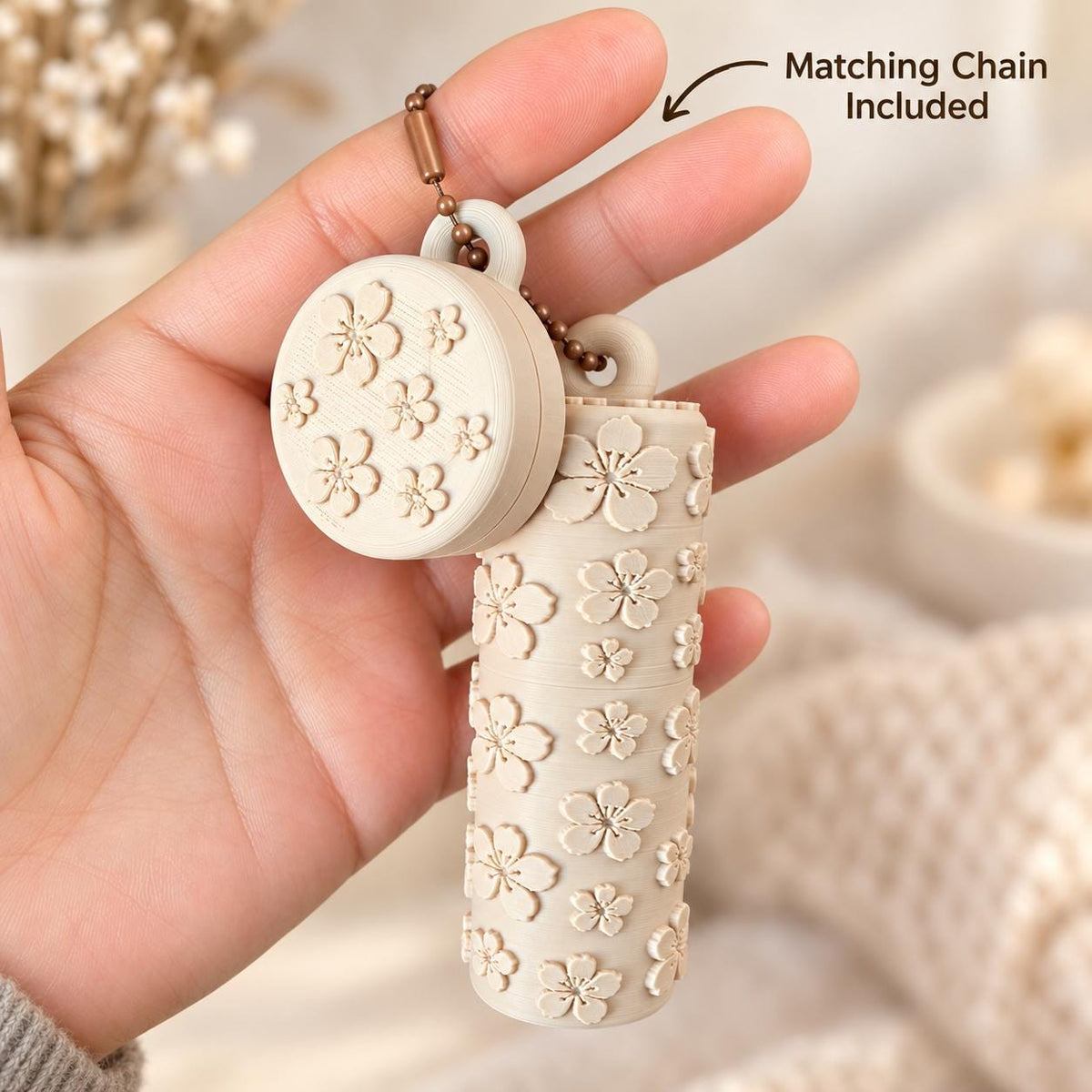 Beige floral lip balm holder and coordinating round ring holder displayed in a hand with the included matching chain.