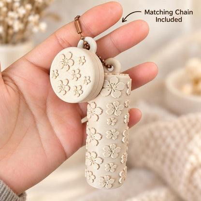 Beige floral lip balm holder and coordinating round ring holder displayed in a hand with the included matching chain.